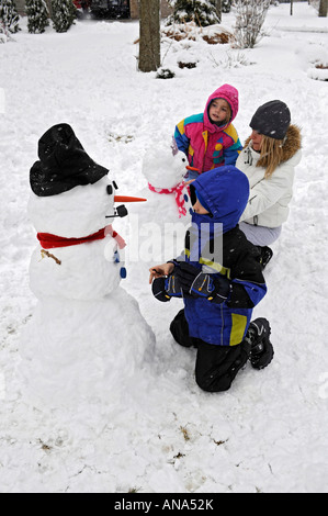 Kinder bauen Schneemann mit Mutter nach einem Winter Schneefall Stockfoto