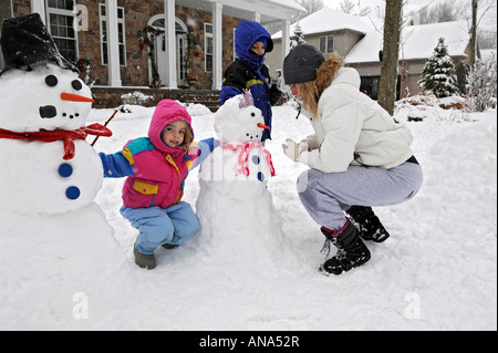 Kinder bauen Schneemann mit Mutter nach einem Winter Schneefall Stockfoto