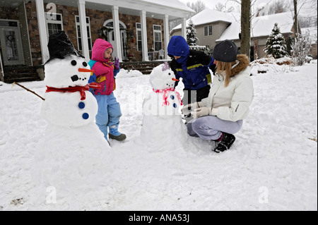 Kinder bauen Schneemann mit Mutter nach einem Winter Schneefall Stockfoto