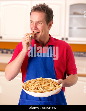MANN IN DER KÜCHE MIT SCHÜSSEL MIT POMMES FRITES Stockfoto
