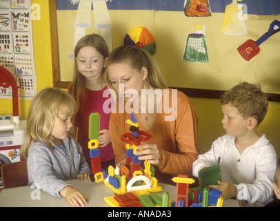 Kinder, die mit „Stickle Bricks“ in der Vorschule spielen, zusammen mit einer Helferin oder Assistentin, Großbritannien Stockfoto