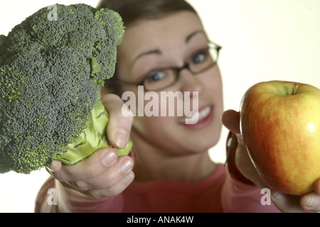 Joung Frau präsentiert einen Apfel und Brokkoli Stockfoto