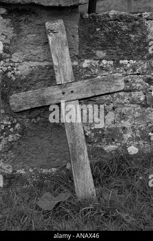 Schwarzweiß-Bild eines alten hölzernen Kreuz Lügen gegen die Wand im Friedhof Stockfoto
