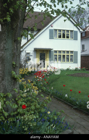 Weg zwischen Frühling Garten grenzt an weißen dreißiger Jahre mit grauen Fensterläden Haus und gelbe Lackierung Stockfoto