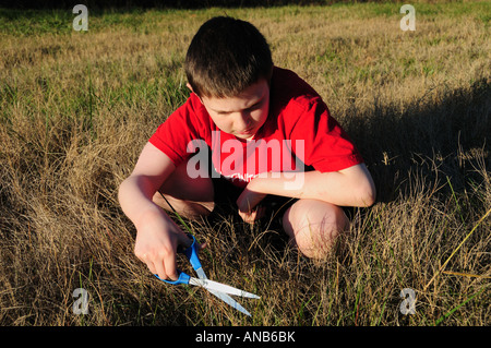 Ein kleiner Junge schneidet dem Rasen der langsame Weg ein Blatt zu einem Zeitpunkt. Symbolisiert das Konzept der harten Detail bei der Arbeit oder eine Verschwendung von Zeit. Stockfoto