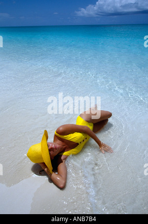 Turks Caicos Provo-Frau im gelben Badeanzug und Hut liegt am Ozean s Rand Stockfoto