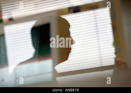 EIN SPIEGELBILD DER MÄNNLICHEN BÜROANGESTELLTEN IN EINEM FENSTER AN SEINEM SCHREIBTISCH Stockfoto