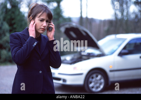 Junge Frau reden über ein Handy mit einem aufgeschlüsselt Auto im Hintergrund Stockfoto