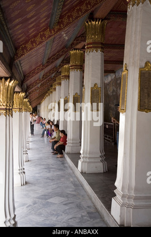 Touristen sitzen in den Kreuzgängen der Innenhof des Wat Phra Kaew, im Komplex des Grand Palace, Bangkok, Thailand Stockfoto