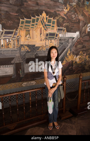 Japanische Touristin, die für ein Foto vor den Ramakianischen Wandmalereien von Wat Phra Kaew posiert, auf dem Gelände des Großen Palastes, Bangkok, Thailand Stockfoto