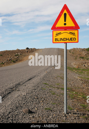 Eine typische Straße in Island mit ein Schild Warnung vor einem blinden Gipfel und zeigt auch Schnee Marker Stockfoto