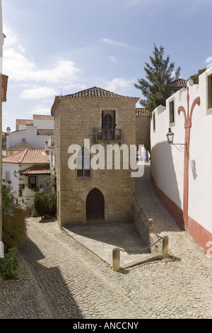 Portugal, Costa da Prata, Estremadura, Obidos mittelalterlichen Stadtmauer. Eine schmale gepflasterte Straße mit einem alten gotischen Haus Stockfoto