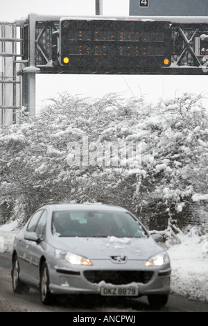 Peugeot Auto mit Scheinwerfern auf der Fahrt entlang behandelten Straße neben Autobahn Warnschild Stockfoto