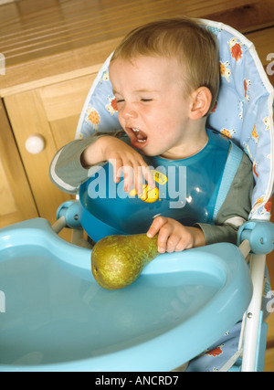 Kleiner Junge sitzen in einen Hochstuhl, der sich weigert zu essen eine Birne Stockfoto