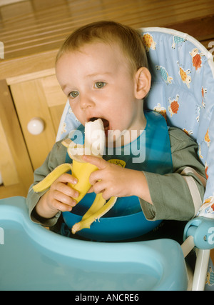 Kleiner Junge in einen Hochstuhl, eine Banane essen hinsetzen Stockfoto