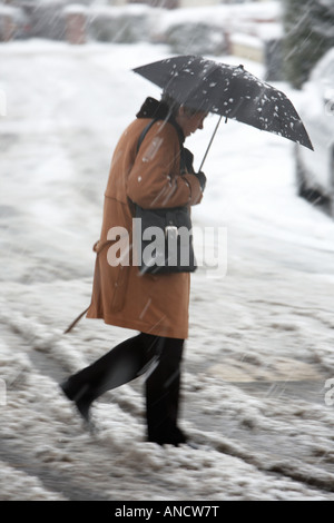 Frau mit Regenschirm geht schnell über schneebedeckte Straße durch Matsch Stockfoto