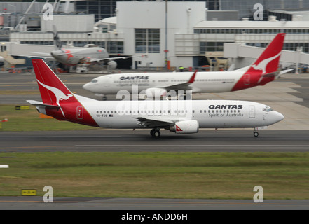 Eine Qantas Boeing 737-400 kommt an einer späteren 737-800 vorbei, während sie die Startbahn hinunter zum Start vom Flughafen Sydney beschleunigt. Flugverkehr an einem belebten Flughafen. Stockfoto