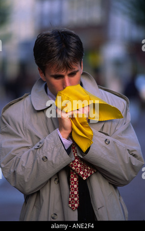 Ein junger Mann niest in ein gelbes Taschentuch. Stockfoto