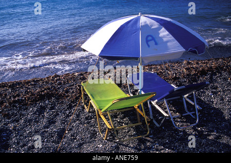 Zwei leere verstellbare Stühle und Sonnenschirm an einem einsamen Strand in Griechenland Stockfoto