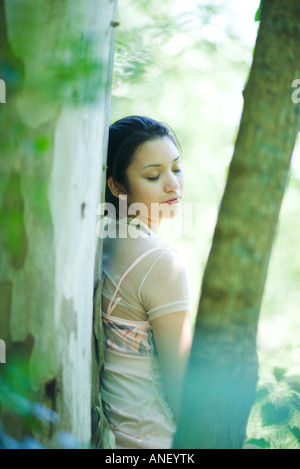 Junge Frau lehnte sich gegen Baum, Augen geschlossen Stockfoto