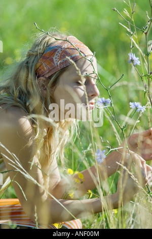 Junge Frau sitzt im Feld, wilde Blumen riechen Stockfoto