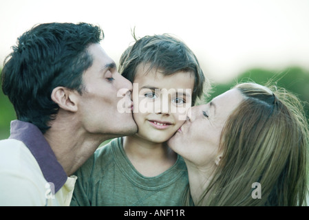 Junge wird von Eltern, in die Kamera Lächeln auf beide Wangen geküsst Stockfoto