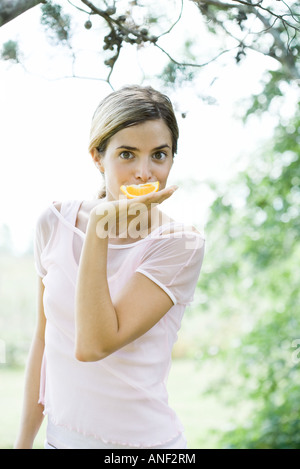 Junge Frau mit Orangenscheibe vor Mund, Blick in die Kamera Stockfoto