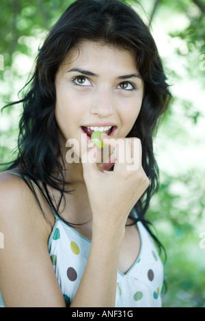 Woman biting into grape, looking up Stockfoto