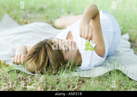 Young woman lying on ground, holding grapes Stockfoto