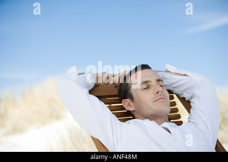 Junger Mann sitzt auf Liegestuhl, Augen geschlossen Stockfoto