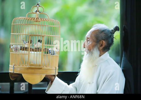 Älterer Mann in traditionelle chinesische Kleidung, Blick auf Vögel im Käfig für Vogel Stockfoto