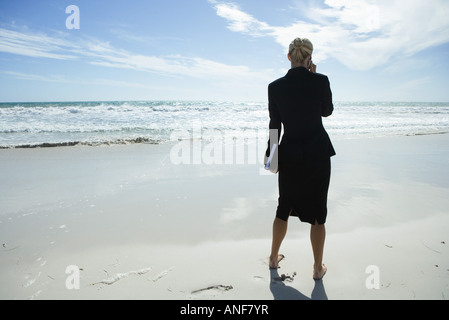 Geschäftsfrau mit Handy, stehen am Strand barfuß, in voller Länge, Rückansicht Stockfoto