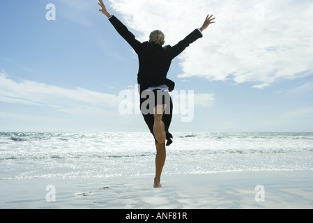 Geschäftsfrau barfuß am Strand, springen in die Luft, Rückansicht Stockfoto