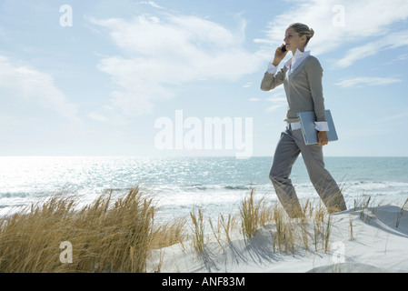 Frau zu Fuß über Dünen, mit Handy, Laptop unter dem Arm tragen Stockfoto