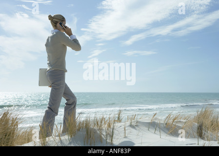 Frau zu Fuß über Dünen, mit Handy, Laptop unter dem Arm tragen Stockfoto