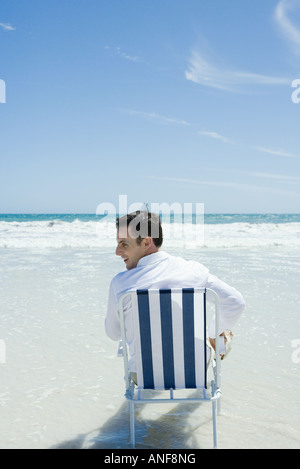 Mann sitzt im Klappstuhl am Strand, Rückansicht Stockfoto