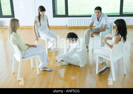 Mann sitzt auf dem Boden in der Mitte der Gruppe sitzen auf Stühlen, im Gespräch Stockfoto