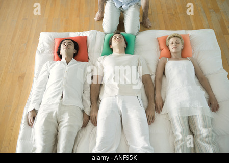 Alternative Therapie-Sitzung, drei Erwachsene nebeneinander liegend, während Therapeutin in der Nähe kniet, beschnitten Stockfoto
