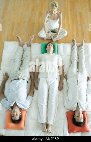 Alternative Therapie-Sitzung, drei Erwachsene nebeneinander liegend, während Therapeuten Hände über den Kopf des Mannes stellt aus Stockfoto