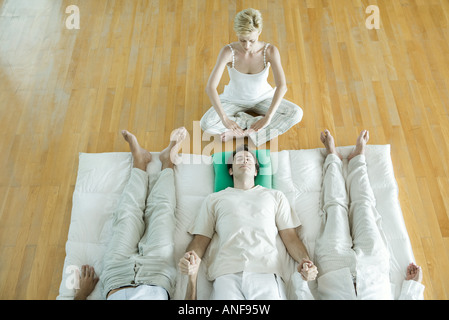 Alternative Therapie-Sitzung, drei Erwachsene nebeneinander liegend, Hand in Hand und Therapeuten Hände über den Kopf des Mannes Stockfoto