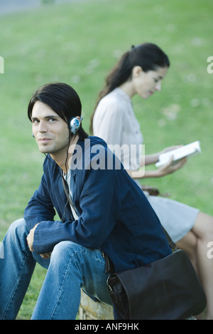 Leute sitzen im Park, Man Kopfhörer anhören, während Frau Buch liest Stockfoto