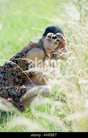 Junge Frau kauert in hohe Gräser, lächelnd in die Kamera Stockfoto