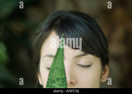 Junge Frau hinter Blatt, Augen geschlossen, beschnitten, Porträt Stockfoto