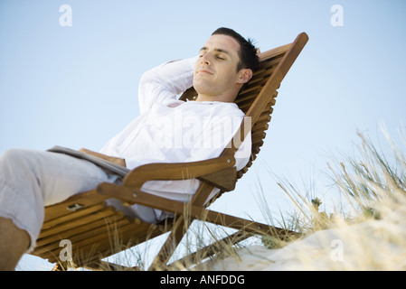 Junger Mann im Liegestuhl sitzen, Lächeln, niedrigen Winkel Ansicht Stockfoto