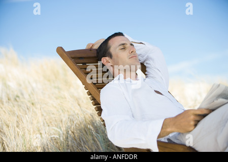 Junger Mann sitzt im Liegestuhl, Nickerchen Stockfoto