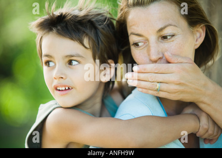 Mutter und Sohn, Frau halten junge auf Rücken, flüstert ihm Stockfoto