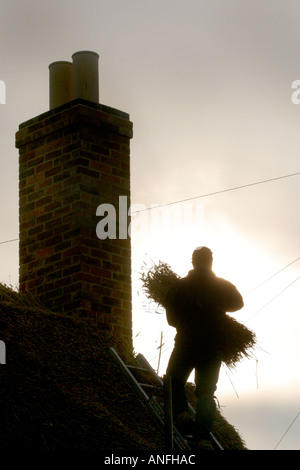 Thatcher am Dach der Hütte Silhouette gegen Sonne Stockfoto