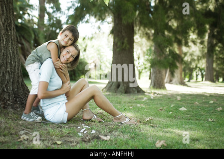Mutter und Sohn sitzen im Freien, umarmt junge Frau von hinten Stockfoto