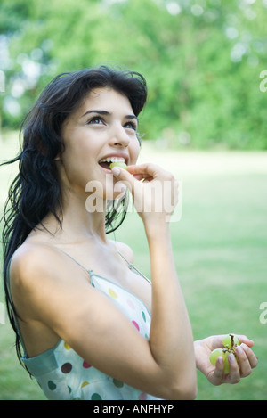 Young woman eating grapes, looking up Stockfoto