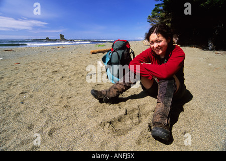 Eine junge Frau (20-25) nimmt eine Auszeit vom Wandern entlang einem Strandabschnitt von der West Coast Trail in der Nähe von Carmanah Creek im Pacific Rim Stockfoto
